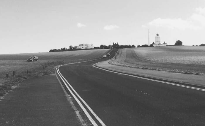 particolare della copertina del libro di Abram Tomasi "Oltre": foto bn con strada americana che corre tra i campi coltivati