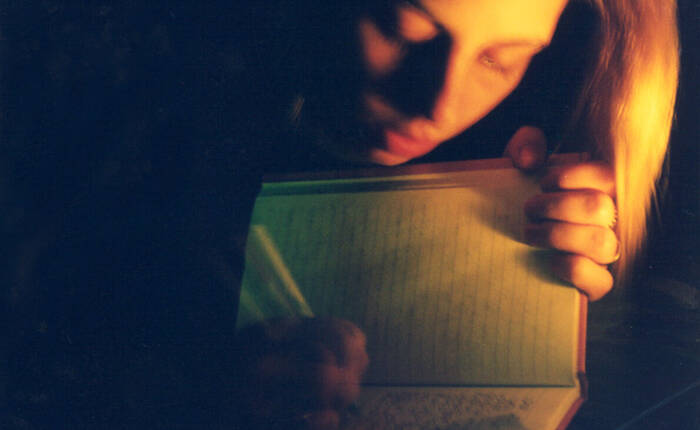 Giovane che scrive su un diario, con luce fioca